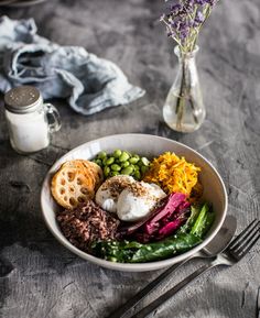 a bowl filled with different types of food next to a fork and glass vase full of flowers