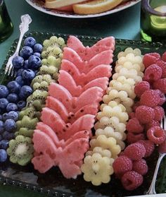 there are many different fruits in the trays on the table with forks and spoons next to each other