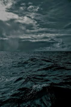 the ocean is dark and stormy with some clouds in the sky above it, as seen from a boat