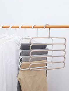 clothes hanging on a rail in front of a white wall and two wooden hangers