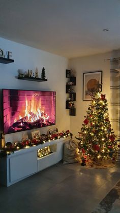 a living room with a christmas tree and fire in the fireplace