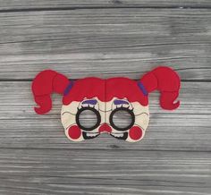 a red and white clown mask sitting on top of a wooden table next to a pair of glasses