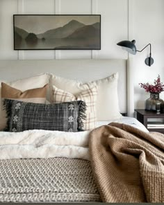 a bed with pillows and blankets on top of it next to a wall mounted painting