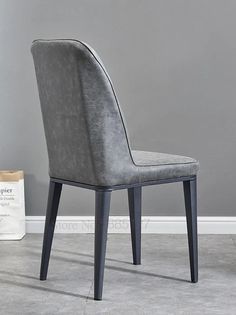 a grey velvet dining chair next to a white bag and gray wall in the background