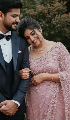 a man in a tuxedo and a woman in a pink dress smile at each other