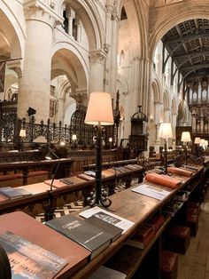 the long tables are lined up in the cathedral with books on them and lamps hanging from the ceiling