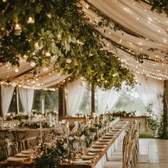 an outdoor tent with tables and chairs covered in greenery