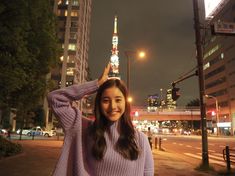 a woman standing on the side of a road in front of tall buildings at night