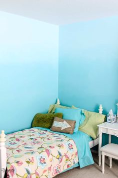 a bedroom with blue walls and green pillows on the bed, along with white furniture