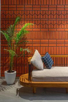 a couch with pillows and a potted plant in front of a red brick wall