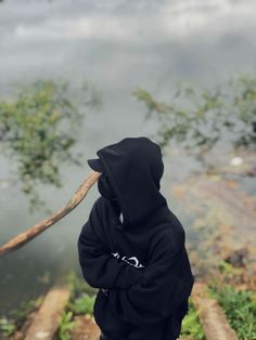 a person in a black hoodie holding a stick over their head and looking at the water