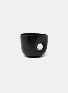 a black bowl sitting on top of a white surface with a hole in the middle