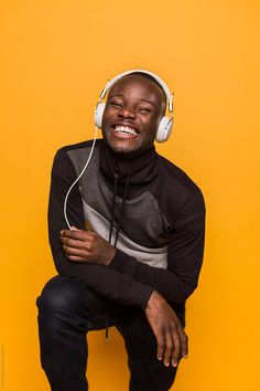 a man wearing headphones sitting on top of a yellow wall with his arms crossed