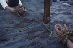 two people are tied up on the beach with ropes and rope around them, while one person holds his hand out