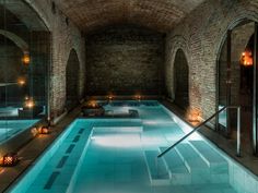 an indoor swimming pool surrounded by brick walls and arched doorways, with candles lit on the floor