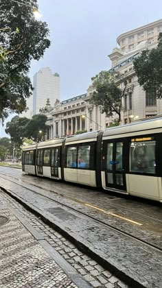 a train traveling down tracks next to a tall building on a city street in the rain