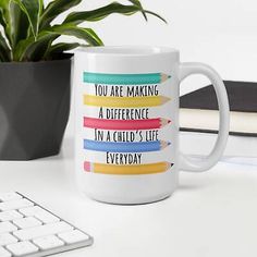 a white coffee mug sitting on top of a desk next to a keyboard and potted plant