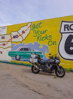 a motorcycle parked in front of a wall with cars and route 66 painted on it