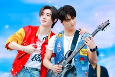 two young men standing next to each other holding guitars