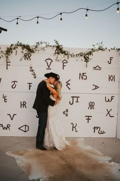 a bride and groom kissing in front of a wall with cursive writing