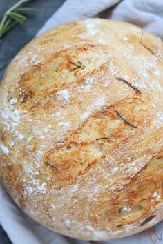 a round loaf of bread sitting on top of a white napkin next to an rosemary sprig