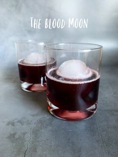 two glasses filled with liquid and ice on top of a gray surface, next to the words'the blood moon '