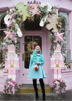 a woman standing in front of a pink building with flowers and decorations on the door