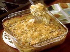 a casserole dish is sitting on a plate with a spoon in it and someone's hand reaching into the casserole