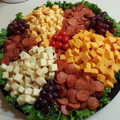 a platter filled with cheese, meats and grapes on top of lettuce