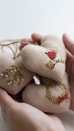 two hands are holding small stuffed animals with embroidered designs on them, and one hand is holding the other