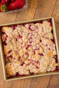 a pan filled with strawberry cobbler next to a bowl of strawberries on a wooden table