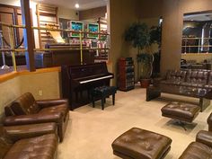 a living room filled with brown leather furniture and a piano in the corner next to a window