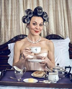 a woman sitting in bed holding a cup and saucer