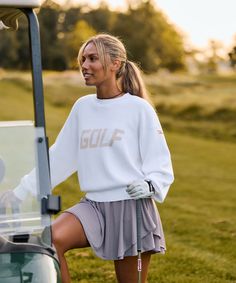 a woman standing next to a golf cart in the grass with her foot up on the driver's wheel