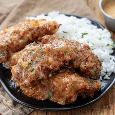 two pieces of fried chicken on a black plate with white rice and gravy