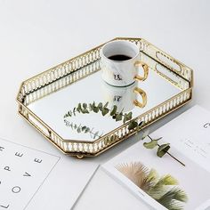 a gold tray with a coffee cup on it next to an envelope and other items