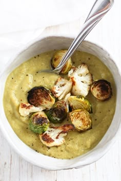 a white bowl filled with broccoli and cauliflower soup on top of a wooden table