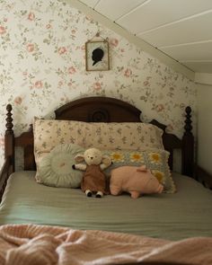 two stuffed animals sit on top of a bed in a room with floral wallpaper