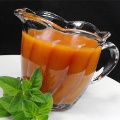 a glass pitcher filled with liquid next to a leafy green plant on a white plate