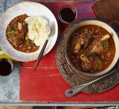 two bowls of stew and mashed potatoes on a red tray with utensils