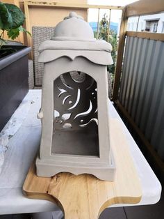 a small white clock sitting on top of a wooden table next to a potted plant