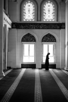 a person standing in an empty room with two large windows and a rug on the floor