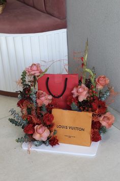 a red bag sitting on top of a table filled with flowers and greenery next to a sign that says louis vuitton