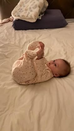 a baby laying on top of a bed next to pillows