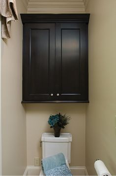 a white toilet sitting in a bathroom next to a wooden cabinet over it's door