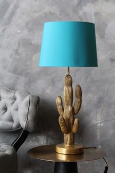 a gold cactus lamp sitting on top of a table next to a gray chair with a blue shade