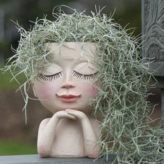 a doll with long hair sitting on top of a wooden bench next to a plant