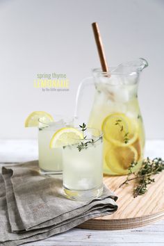 two glasses filled with lemonade sitting on top of a wooden table next to a pitcher