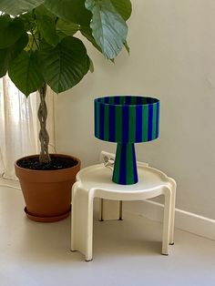 a table with a lamp on it next to a potted plant and a chair