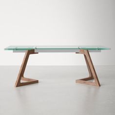 a glass table with wooden legs on a concrete floor in front of a white wall